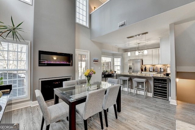 dining space featuring wine cooler, light wood-style flooring, visible vents, baseboards, and a glass covered fireplace