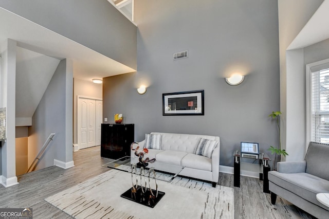 living area with light wood-type flooring, baseboards, a high ceiling, and visible vents