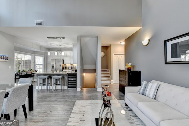 living area with visible vents, baseboards, wine cooler, stairs, and light wood-style floors