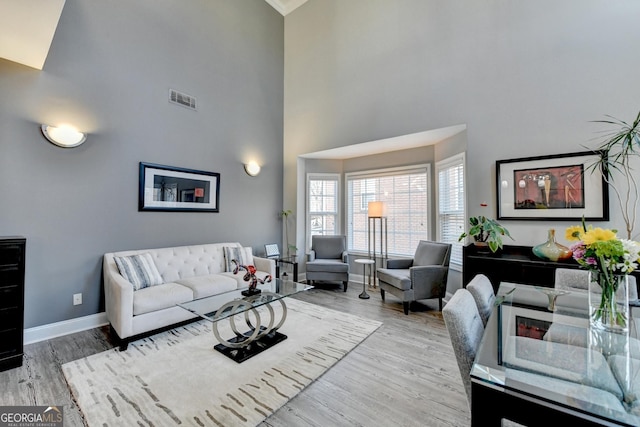 living room with light wood-style floors, visible vents, a towering ceiling, and baseboards