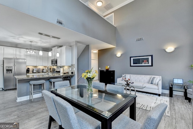 dining room with a high ceiling, light wood-type flooring, visible vents, and baseboards