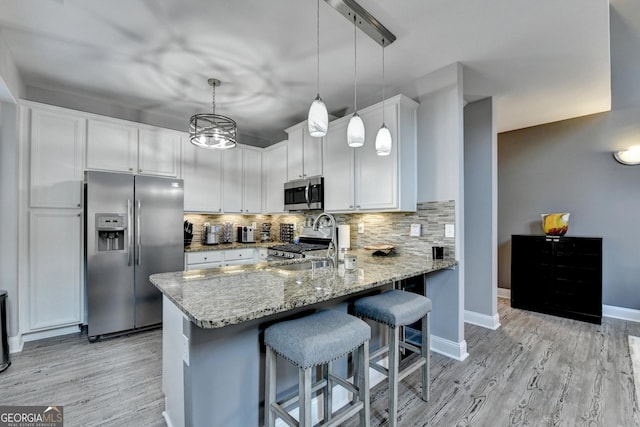 kitchen featuring stainless steel appliances, hanging light fixtures, white cabinetry, a sink, and a peninsula