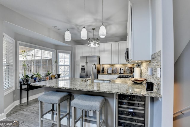 kitchen with beverage cooler, white cabinetry, hanging light fixtures, appliances with stainless steel finishes, and light stone countertops