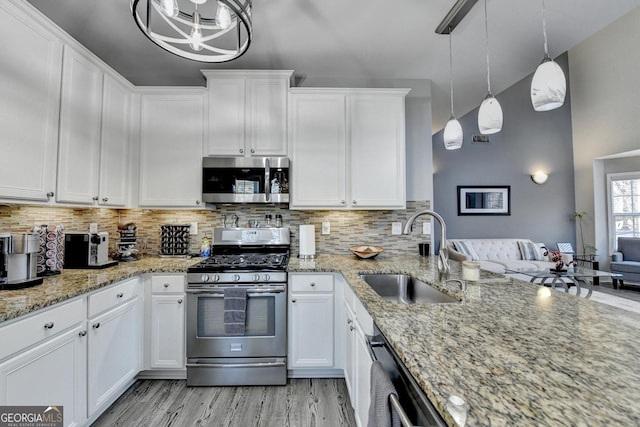 kitchen featuring stainless steel appliances, hanging light fixtures, white cabinetry, a sink, and light stone countertops