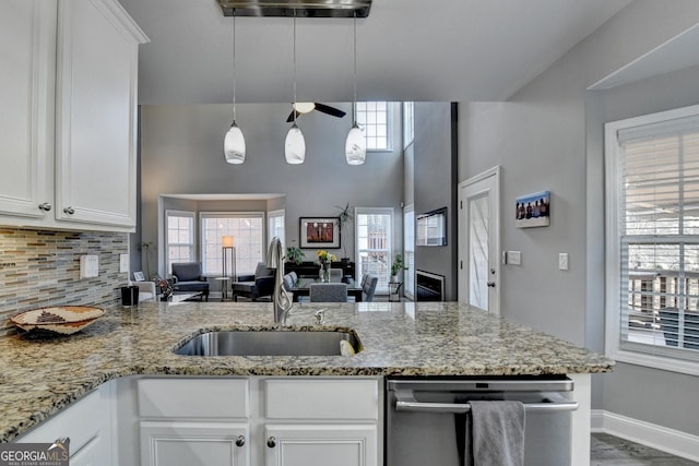 kitchen featuring a peninsula, stainless steel dishwasher, light stone countertops, and white cabinets