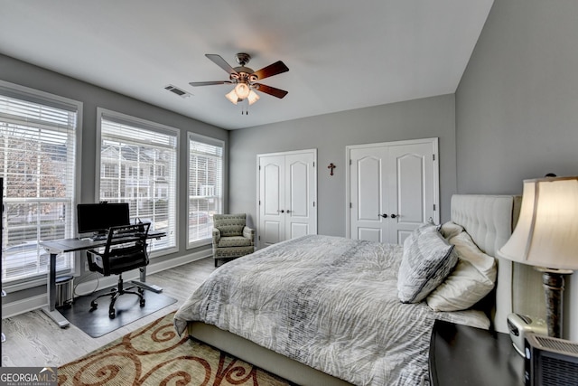 bedroom with light wood-type flooring, ceiling fan, visible vents, and multiple closets