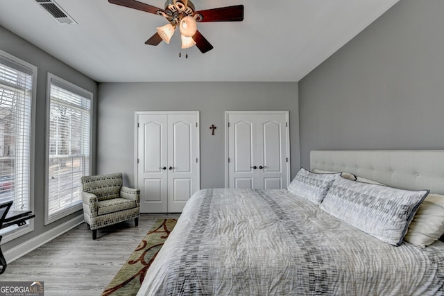 bedroom featuring baseboards, visible vents, ceiling fan, light wood-style floors, and two closets