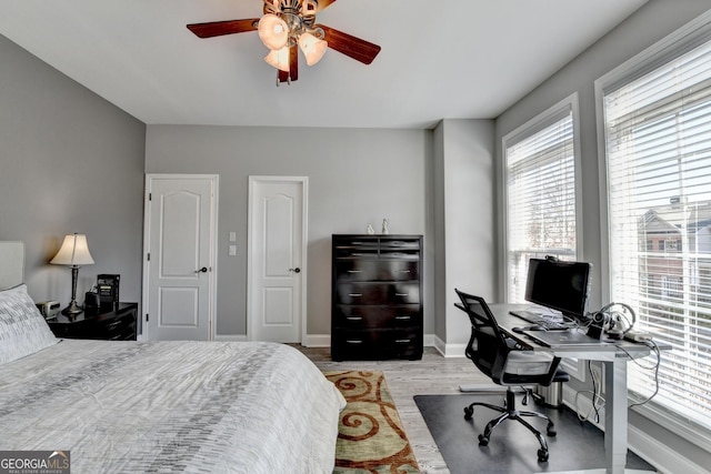 bedroom with a ceiling fan, light wood-type flooring, multiple windows, and baseboards