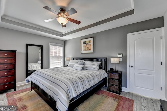 bedroom with light wood-style floors, baseboards, a tray ceiling, and ceiling fan