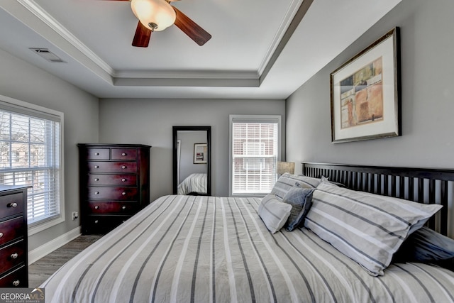 bedroom featuring dark wood-style flooring, a tray ceiling, multiple windows, and baseboards