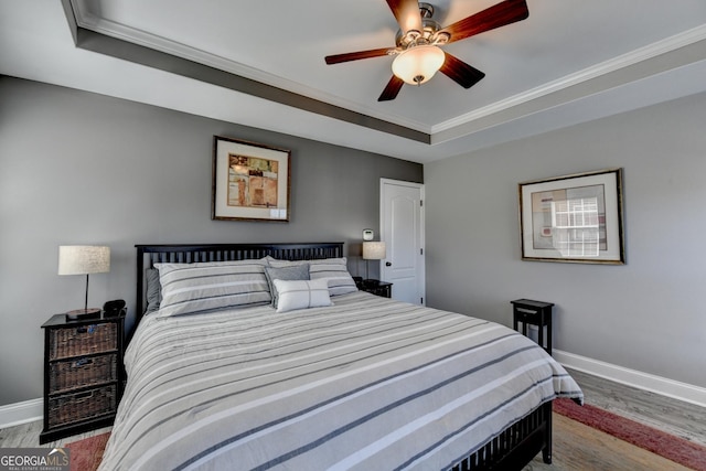 bedroom featuring ceiling fan, wood finished floors, baseboards, ornamental molding, and a raised ceiling