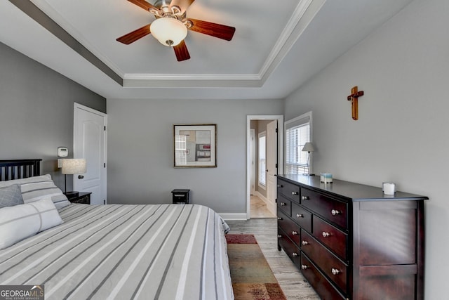 bedroom featuring light wood-style flooring, crown molding, a tray ceiling, and baseboards