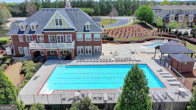 back of property with a patio area, a community pool, fence, and brick siding