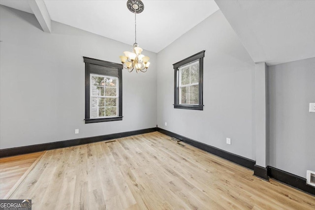 empty room featuring lofted ceiling, plenty of natural light, light hardwood / wood-style floors, and a chandelier