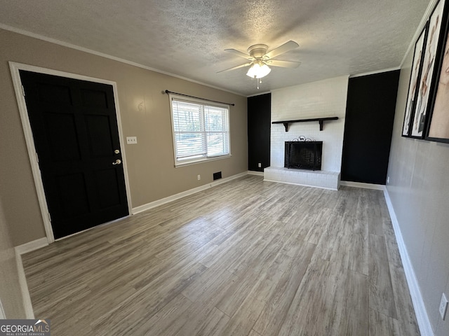 unfurnished living room with ceiling fan, ornamental molding, light hardwood / wood-style floors, a textured ceiling, and a brick fireplace