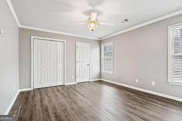 unfurnished bedroom with ceiling fan, multiple closets, crown molding, and dark hardwood / wood-style floors