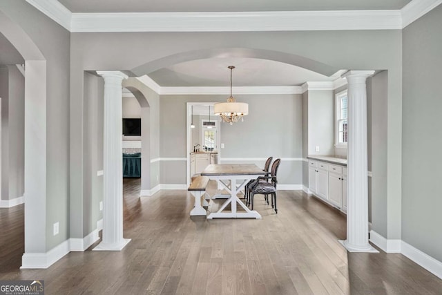 dining area with ornate columns, a chandelier, crown molding, and hardwood / wood-style floors