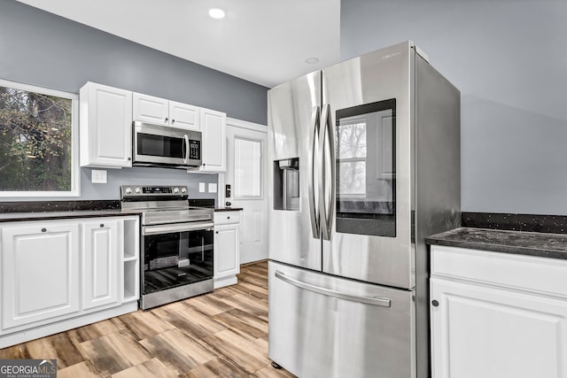 kitchen featuring white cabinetry, stainless steel appliances, light hardwood / wood-style floors, and dark stone counters