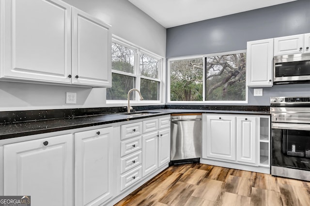 kitchen with sink, white cabinetry, appliances with stainless steel finishes, dark stone counters, and light hardwood / wood-style floors