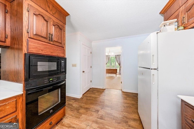 kitchen featuring crown molding, a notable chandelier, black appliances, a textured ceiling, and light wood-type flooring