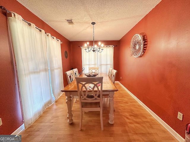 dining room with a notable chandelier, light wood finished floors, visible vents, a textured ceiling, and baseboards