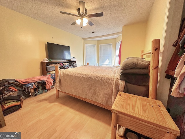 bedroom with a ceiling fan, visible vents, a textured ceiling, and wood finished floors