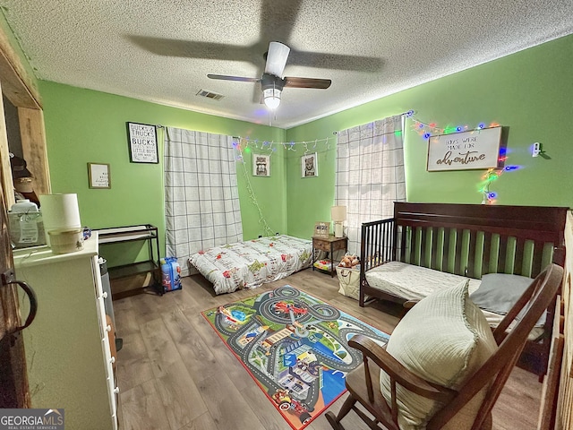 bedroom with visible vents, ceiling fan, a textured ceiling, and wood finished floors