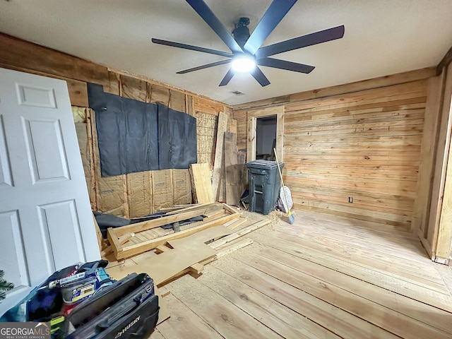 spare room with a wood stove, wood walls, wood-type flooring, and ceiling fan