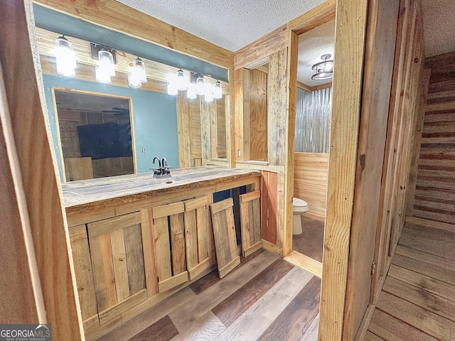 bathroom featuring a textured ceiling, toilet, wooden walls, wood finished floors, and vanity