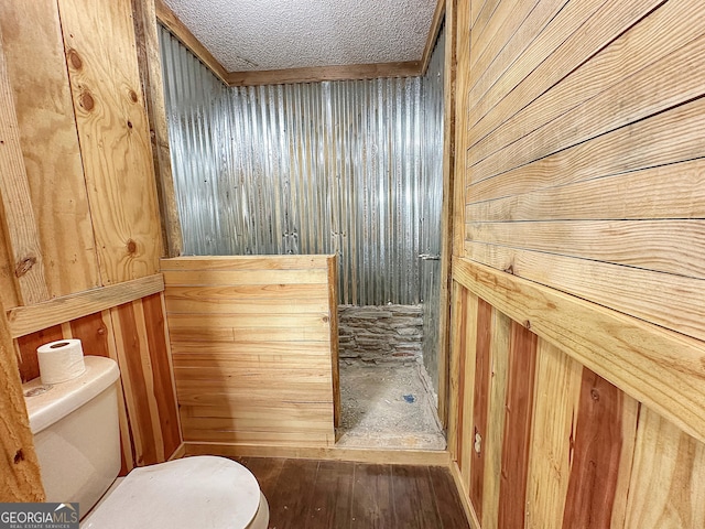 bathroom with wood walls, a shower stall, toilet, and wood finished floors