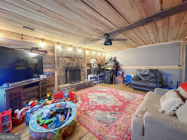 living area featuring wood ceiling, wood-type flooring, a ceiling fan, and a stone fireplace