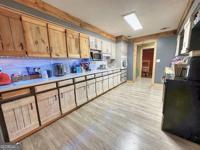 kitchen featuring light countertops, white oven, stainless steel microwave, and light wood-style flooring