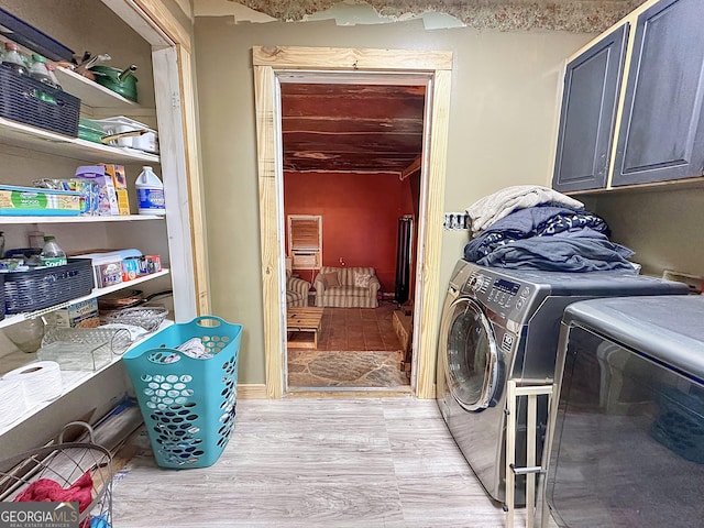 washroom featuring light wood-style flooring, washing machine and dryer, and cabinet space