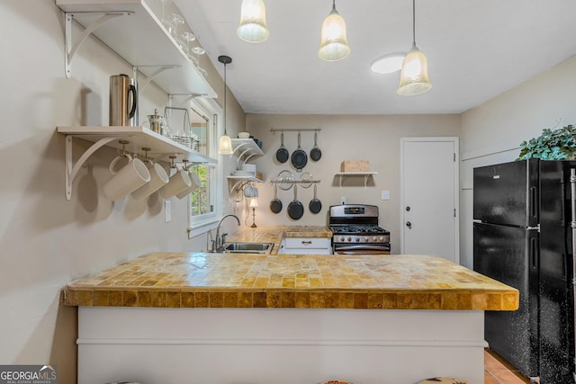 kitchen with sink, gas stove, decorative light fixtures, black refrigerator, and kitchen peninsula