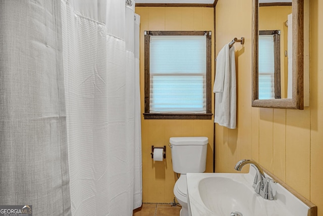 bathroom with toilet, tile patterned flooring, sink, and wood walls