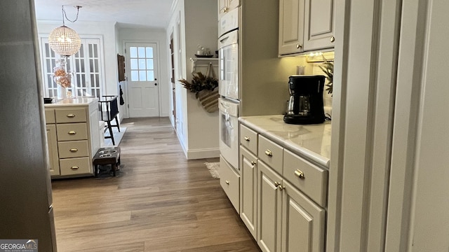 kitchen with cream cabinets, decorative light fixtures, and light hardwood / wood-style flooring