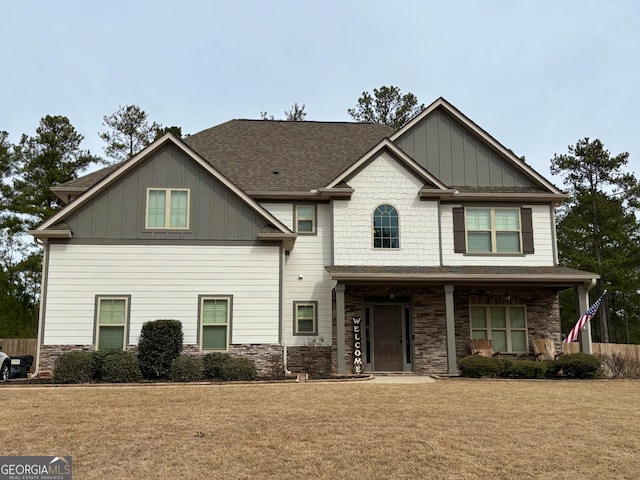 craftsman-style home with stone siding, a front lawn, board and batten siding, and roof with shingles