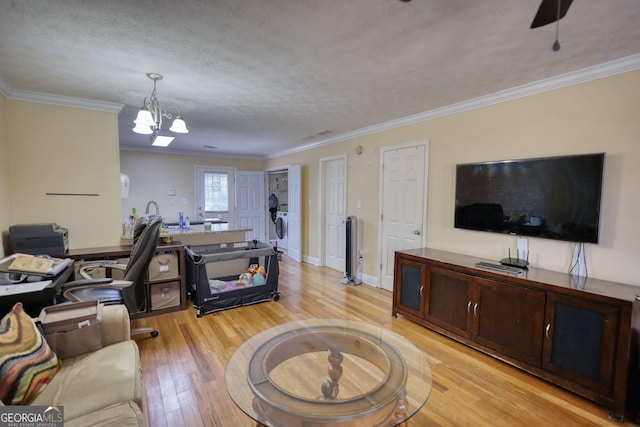 living area featuring a chandelier, a textured ceiling, baseboards, light wood finished floors, and crown molding