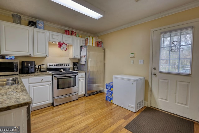 kitchen featuring stainless steel appliances, light countertops, ornamental molding, light wood-style floors, and white cabinetry