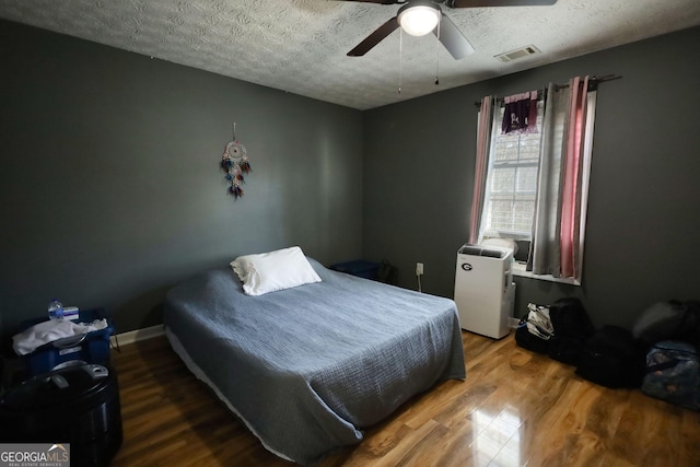 bedroom with a textured ceiling, ceiling fan, wood finished floors, visible vents, and baseboards