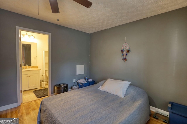 bedroom featuring baseboards, connected bathroom, a textured ceiling, light wood-style floors, and a sink