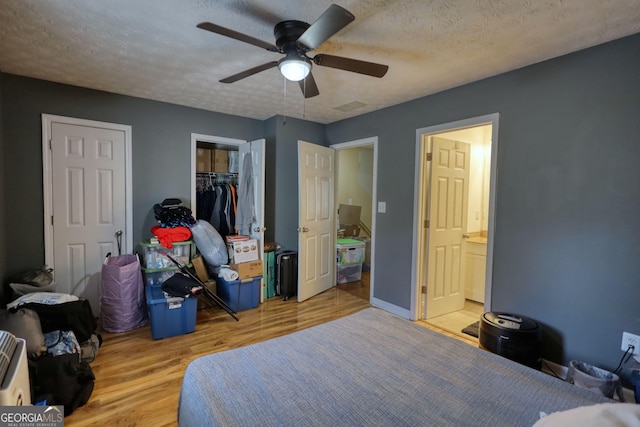 bedroom with a textured ceiling, ensuite bath, wood finished floors, and a ceiling fan