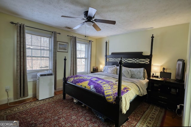 bedroom with visible vents, a ceiling fan, a textured ceiling, wood finished floors, and baseboards