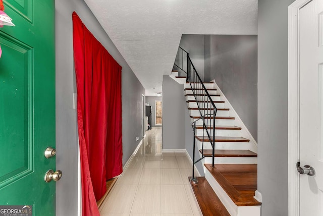 entrance foyer featuring a textured ceiling, stairway, baseboards, and tile patterned floors