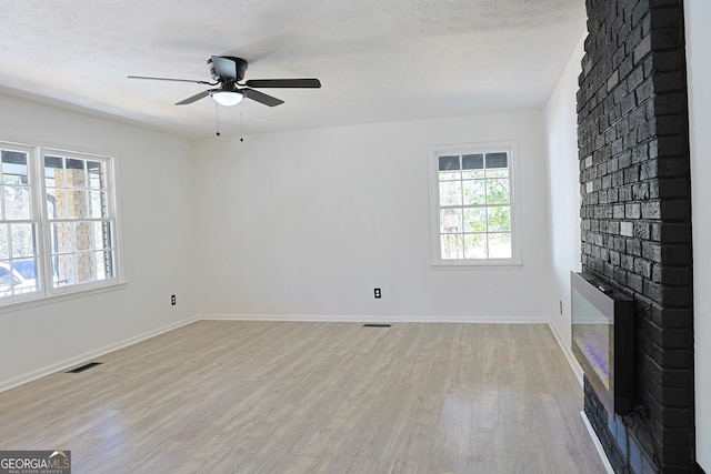 unfurnished living room featuring a fireplace, visible vents, light wood-style floors, a textured ceiling, and baseboards