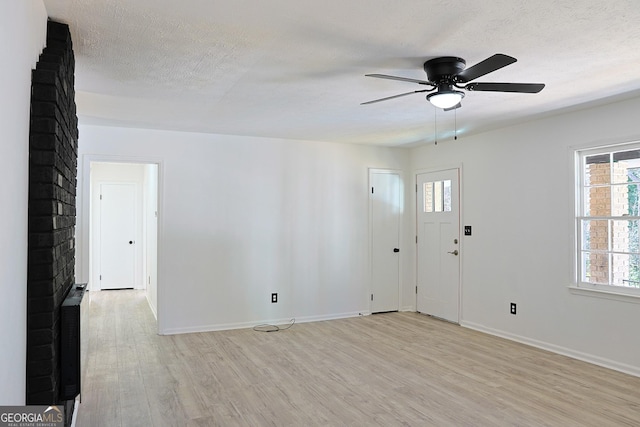 interior space featuring light wood-type flooring, a ceiling fan, baseboards, and a textured ceiling