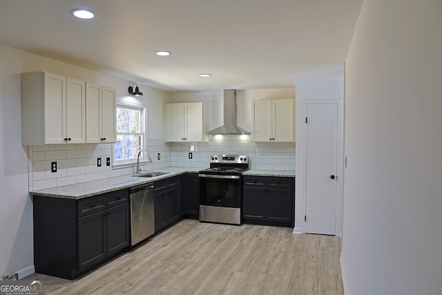 kitchen featuring stainless steel appliances, light wood-style flooring, a sink, light stone countertops, and wall chimney exhaust hood