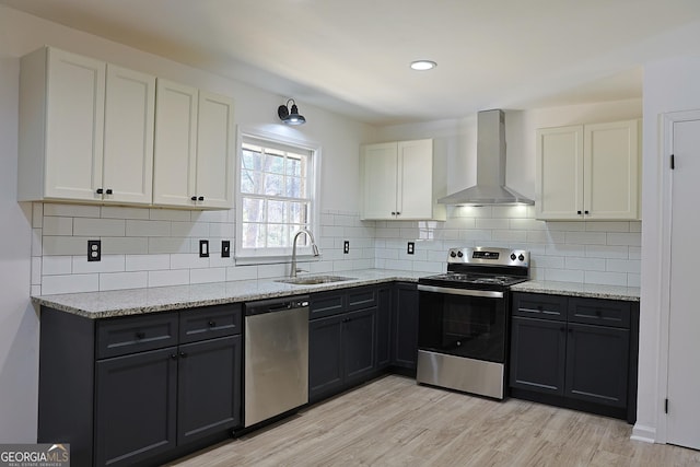 kitchen featuring light stone countertops, wall chimney exhaust hood, appliances with stainless steel finishes, and a sink