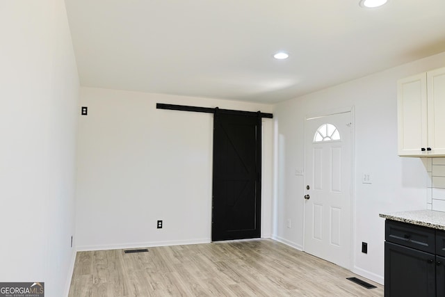 interior space with light wood finished floors, a barn door, light stone counters, and white cabinets