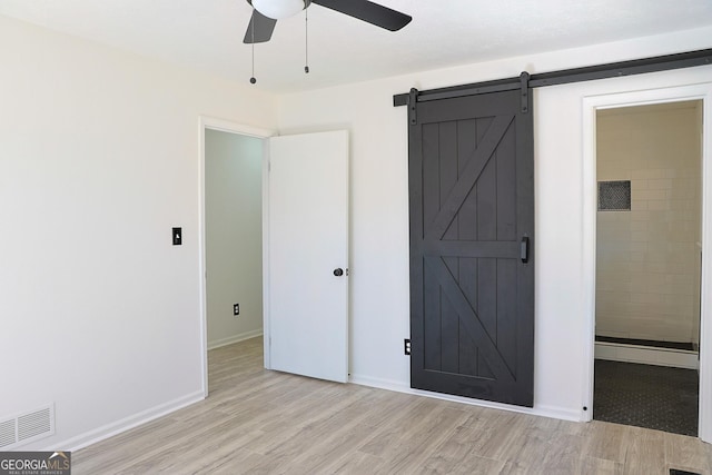 unfurnished bedroom with visible vents, light wood-style flooring, a barn door, a ceiling fan, and baseboards